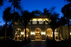 a large white building with palm trees in front of it at night and lit up by lights