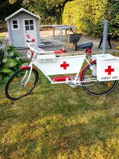 a bike with a red cross painted on it parked in the grass next to a shed