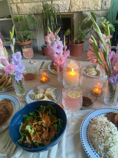 a table topped with plates and bowls filled with food next to candlelight votives