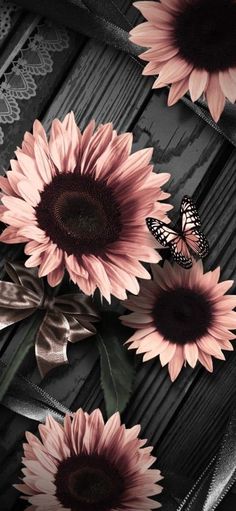 some pink sunflowers and a butterfly on a wooden table with lace around them