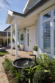 an outdoor fountain in front of a house with white sidings and plants around it