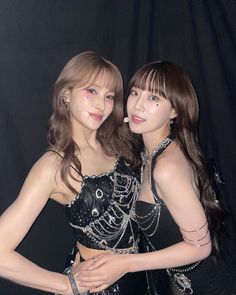 two young women posing for the camera in front of a black background, with one holding her arm around the other's shoulder