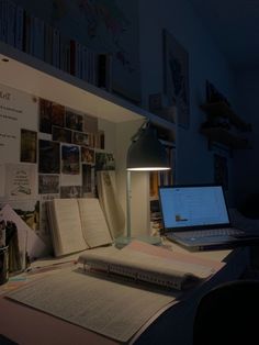 a laptop computer sitting on top of a desk next to a lamp and bookshelf