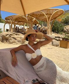 a woman sitting on top of a wooden bench next to an umbrella covered beach area