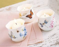 three tea light candles sitting on top of a pink napkin next to a white cup