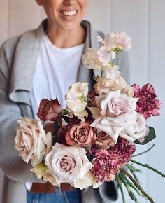 a woman holding a bouquet of flowers in her hands with a smile on her face