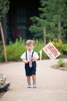 a young boy in blue shorts and tie holding a sign