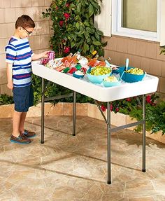 a young boy standing in front of a table with food on it and plants around