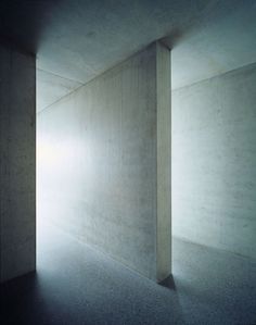 an empty room with light coming in from the ceiling and concrete walls on either side