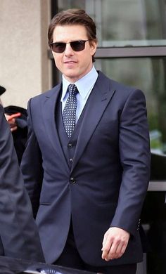 a man in a suit and sunglasses walking out of a building