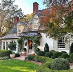 a white house with lots of trees and bushes around it's front door, surrounded by green grass