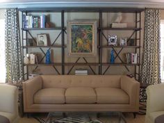 a living room filled with furniture and bookshelves next to a window covered in curtains