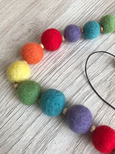 a multicolored felt bead necklace with wooden beads and leather cord on a white wood surface