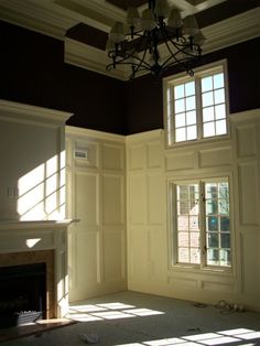 an empty room with a chandelier, fireplace and windows in the middle of it