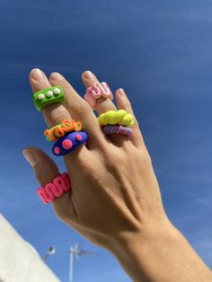 a person's hand with four different colored rings on their fingers and the sky in the background