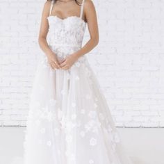 a woman standing in front of a brick wall wearing a white dress with flowers on it