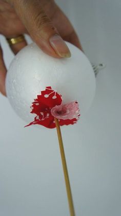 a hand holding a white ball with red flowers on it and a stick sticking out of it