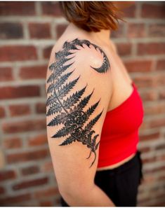 a woman wearing a red top has a fern tattoo on her left arm and shoulder