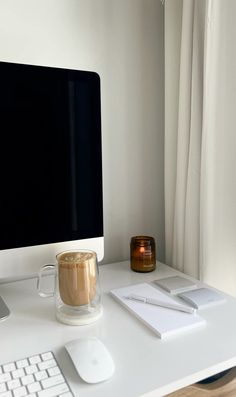 a white desk with a computer monitor, keyboard and mouse next to a cup of coffee