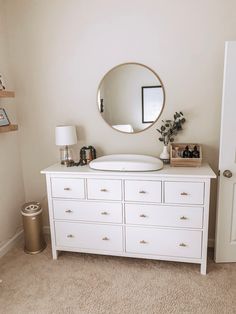 a white dresser with a round mirror above it