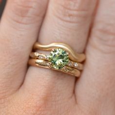 a woman's hand with two gold rings and a green diamond ring on it