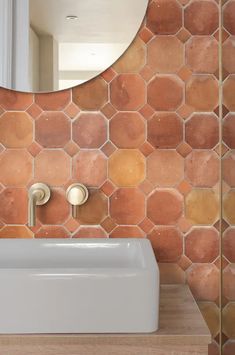 a bathroom sink sitting under a mirror next to a wall mounted faucet in front of a tiled wall