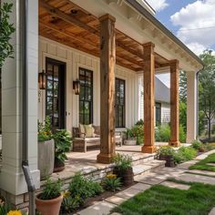 the front porch is covered with wooden pillars and columns, along with potted plants