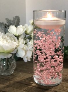 a glass vase filled with pink and white flowers on top of a wooden table next to a candle