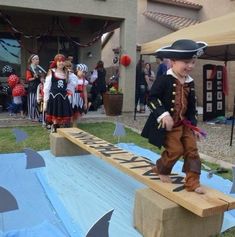 a young boy dressed in pirate clothing standing on a wooden bench with people watching from the background