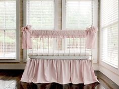 a baby crib with pink ruffled bedding and matching window shades in a white room