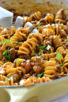 a skillet filled with pasta and meat covered in sauce, garnished with parsley