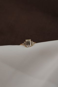 an emerald cut diamond ring sits on a white cloth