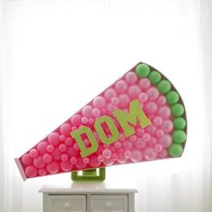 a large pink and green megaphone on top of a white dresser next to a window