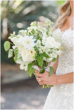 a woman holding a bouquet of white flowers in her hands and wearing a wedding dress