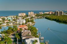 an aerial view of houses and boats on the water in front of a city with palm trees