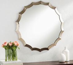 a mirror sitting on top of a dresser next to a vase with flowers in it