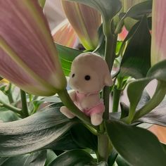 a small stuffed animal sitting on top of a green plant with pink flowers in the background