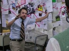 a man in a tie pointing at papers on a wall with writing all over it