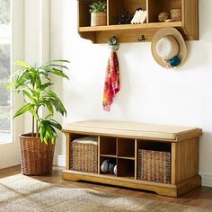 a wooden shelf with baskets and hats on it next to a potted plant in front of a window