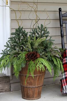 a potted plant with pine cones and greenery sits on the porch next to a rocking chair