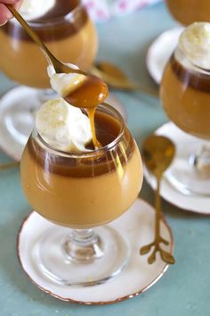 two glasses filled with caramel pudding and topped with whipped cream, spoons and honey