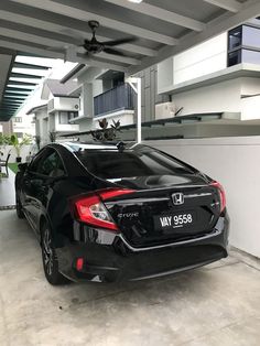 a black car parked in a garage next to a white wall and ceiling fan on top of it