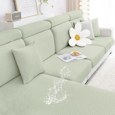 a living room with a green couch and white flowers on the back end, in front of a window