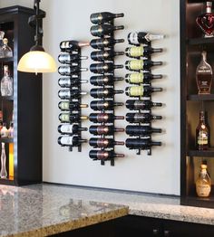 a wall mounted wine rack filled with lots of bottles next to a lamp and counter top