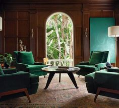 a living room with green chairs and a table in front of a large window that looks out onto the jungle