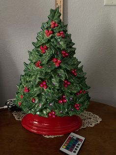 a ceramic christmas tree with red berries on it and a remote control next to it