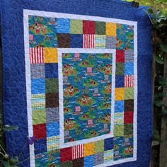 a quilted wall hanging on the side of a fence with trees in the background