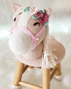 a crocheted toy horse sitting on top of a wooden stool with a pink flower in it's hair