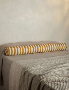 a bed with a striped pillow on top of it next to a white wall and lamp