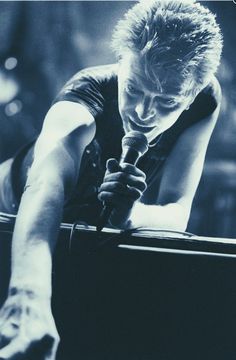 a young man holding a microphone in his right hand and looking down at the ground